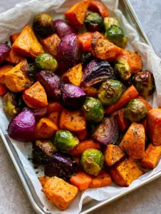 Close up view of charred Brussels sprouts and caramelized sweet potatoes on a silver sheet pan for Sheet Pan Roasted Vegetables recipe.