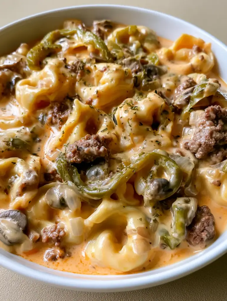Crockpot Cheesesteak Tortellini with Creamy Sauce 1 Detailed view of sauteed mushrooms and translucent onions mixed into the Crockpot Cheesesteak Tortellini pasta dish.